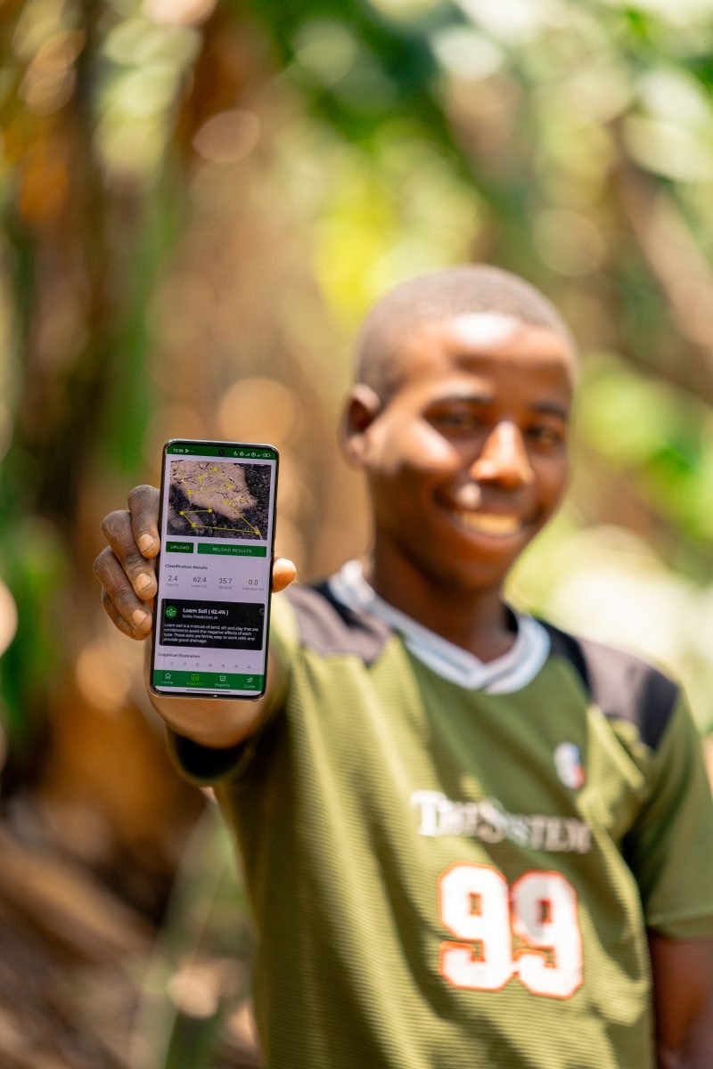 A young farmer smiling as he shows the Soilla app on his phone in Rukungiri