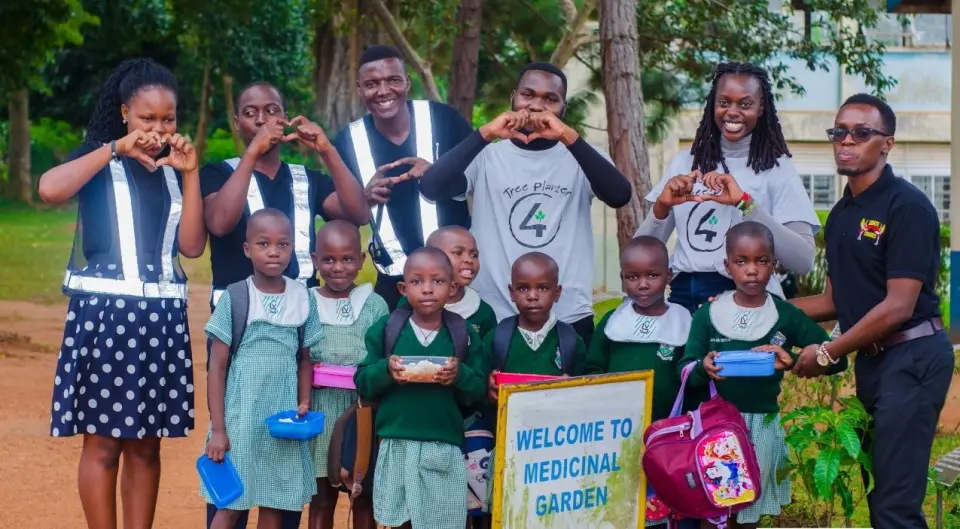 Pupils holding their lunch boxes with our team beside a sign that reads Welcome to Medicinal Garden