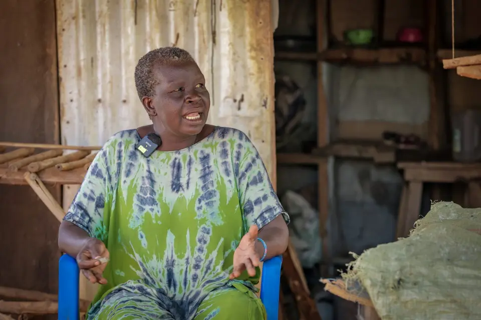 An older woman smiling outside her shop in Yumbe