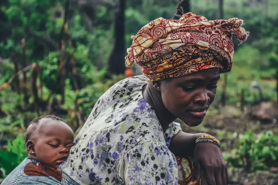 A mother carrying her baby in a farm field