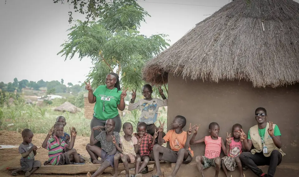 Two BetterLife team members laughing with a group of children outside a home