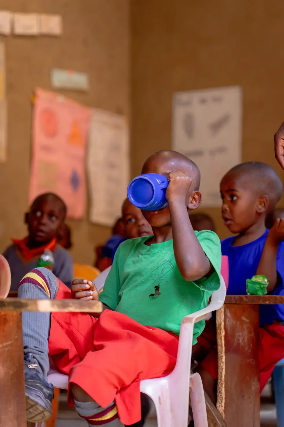 A pupil in a green shirt drinking from a blue cup in class
